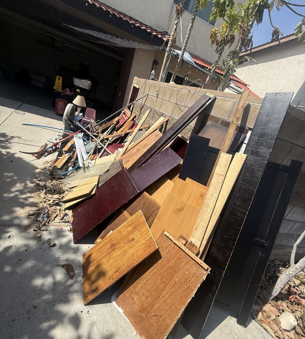 Broken furniture and wood debris stacked by a garage