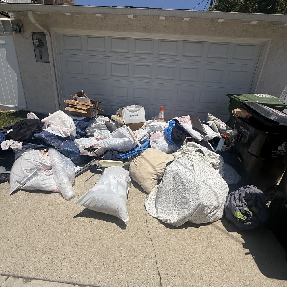Bags and bulky junk piled in front of a garage before pickup in Downey